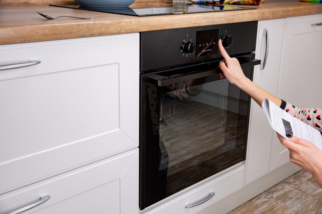 kobieta wybiera program pieczenia w piekarniku z instrukcją w ręku