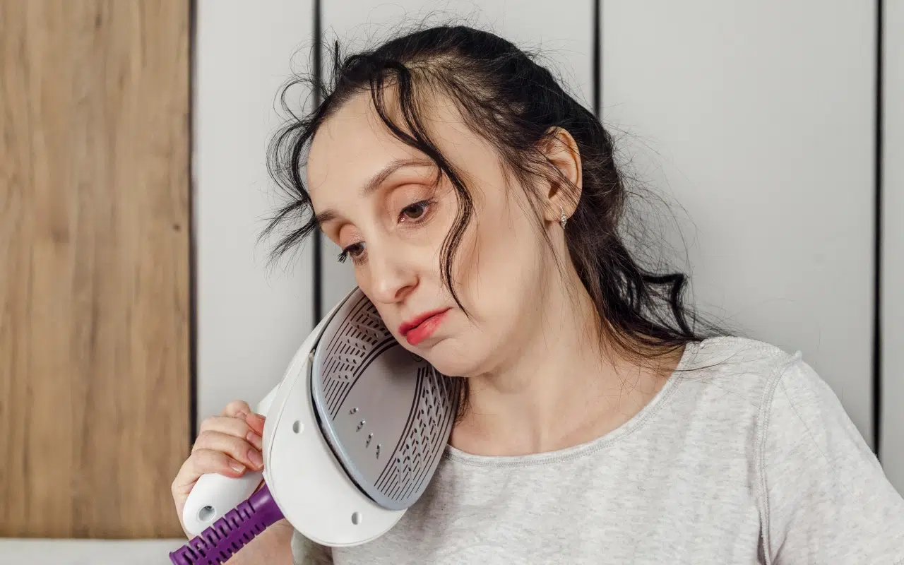 zmęczona obowiązkami domowymi kobieta przykłada do ucha rozgrzane żelazko zamiast telefonu