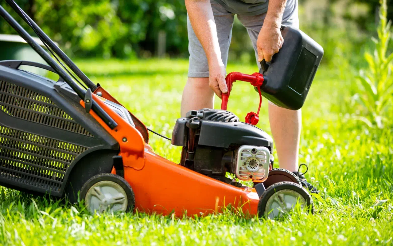 mężczyzna tankuje z kanistra spalinową kosiarkę do trawy