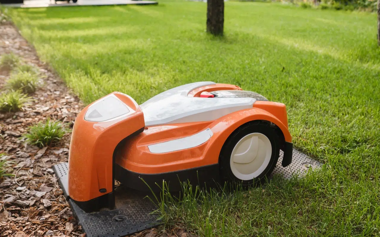 domek dla robota koszącego, w którym ładuje się pomarańczowa kosiarka samojezdna