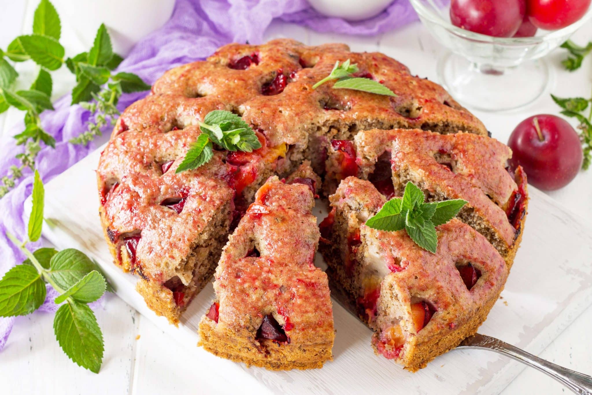 placek owocowy na kuchennym blacie otoczony świeżą miętą i śliwkami