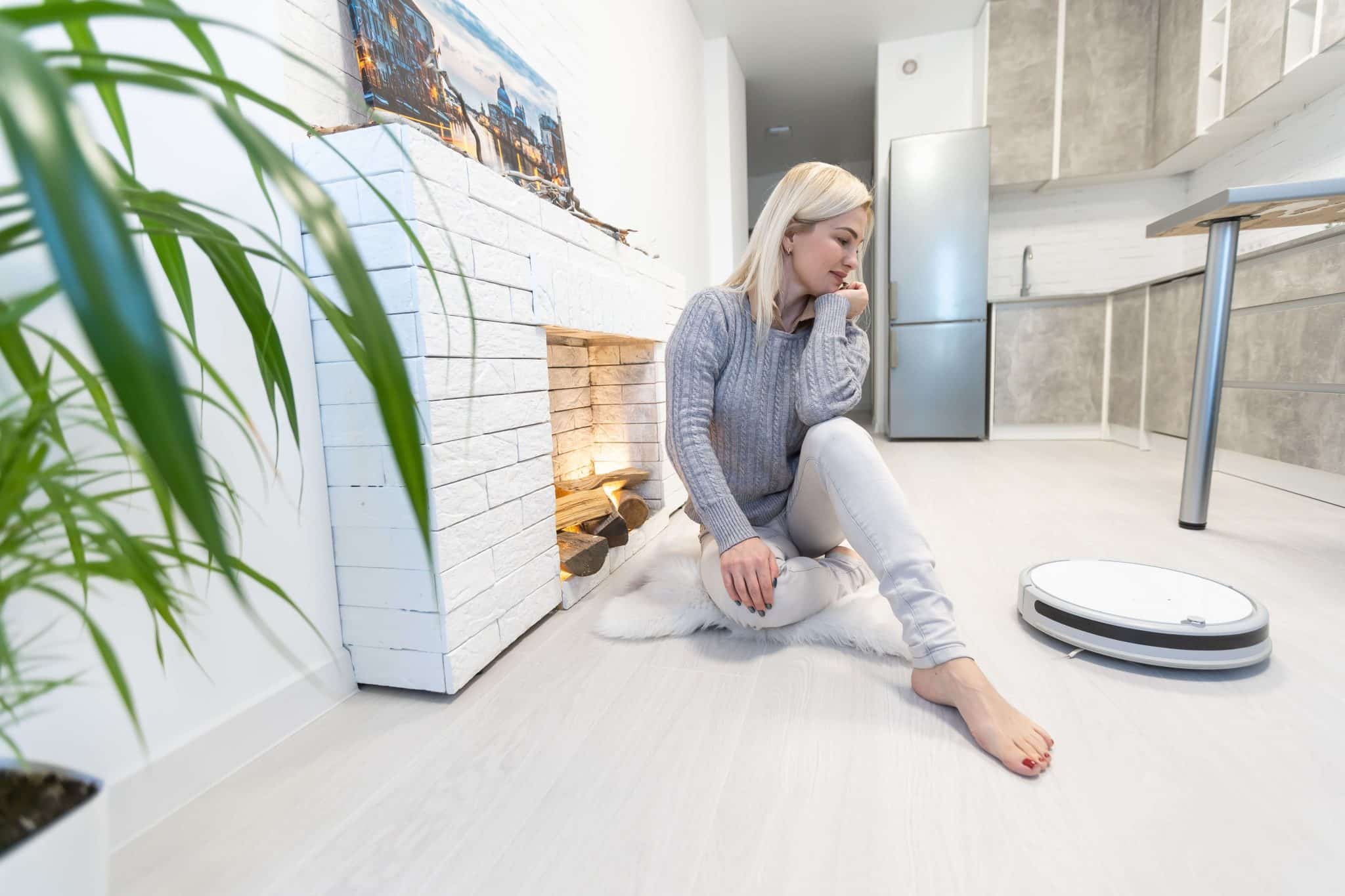 Młoda kobieta siedzi przy kominku w salonie i obserwuje robot sprzątający