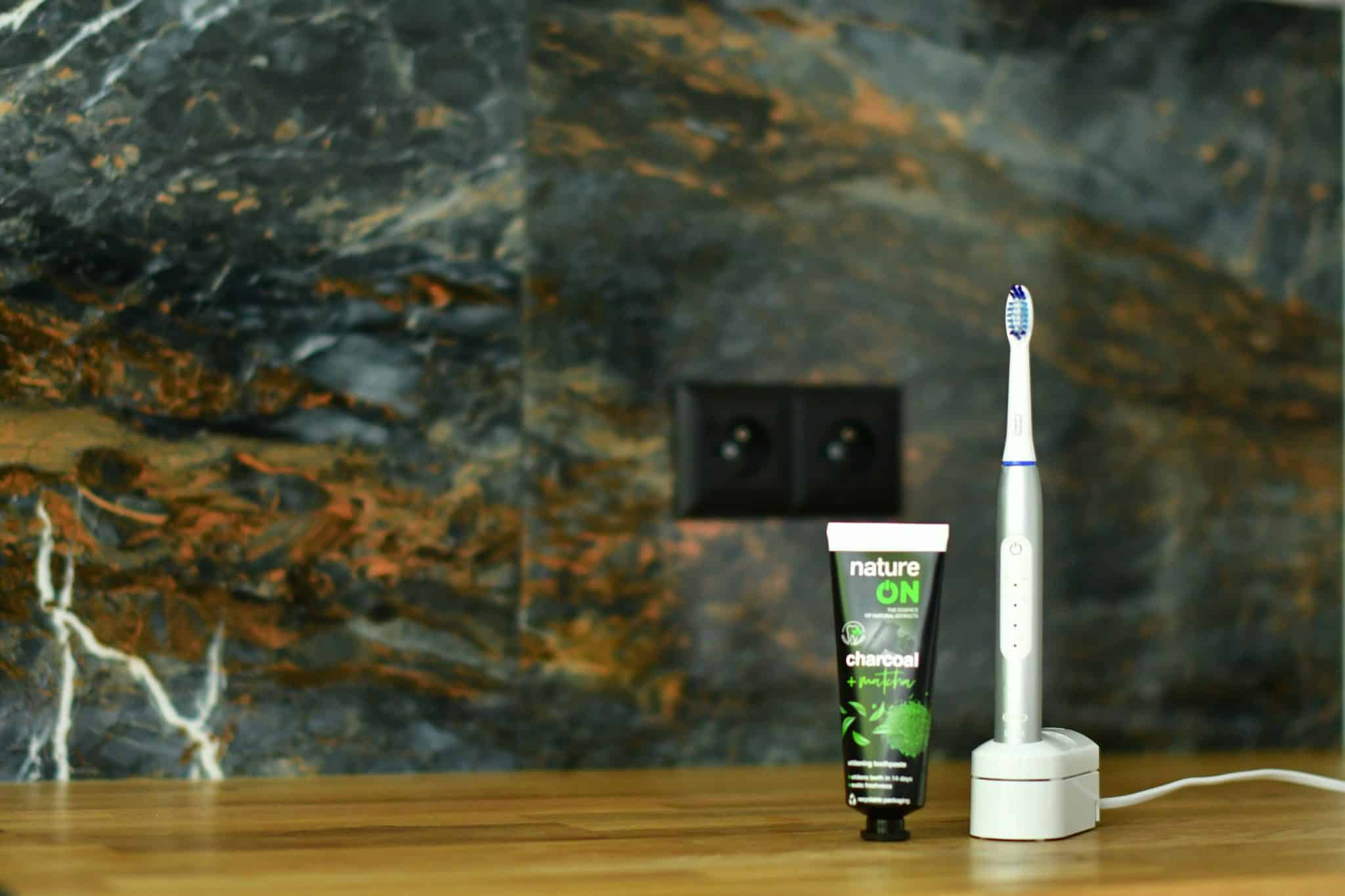 Szczoteczka Oral-B Pulsonic Slim Luxe 4200 na podstawce ładującej, obok tubka pasty do zębów