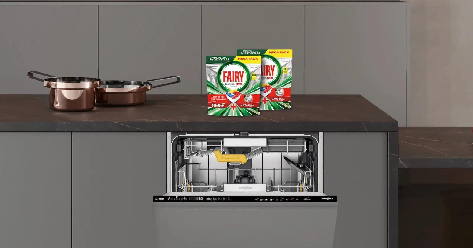 2 opakowania kapsułek Fairy Platinium Plus stoją na kuchennym blacie nad otwartą zmywarką Whirlpool