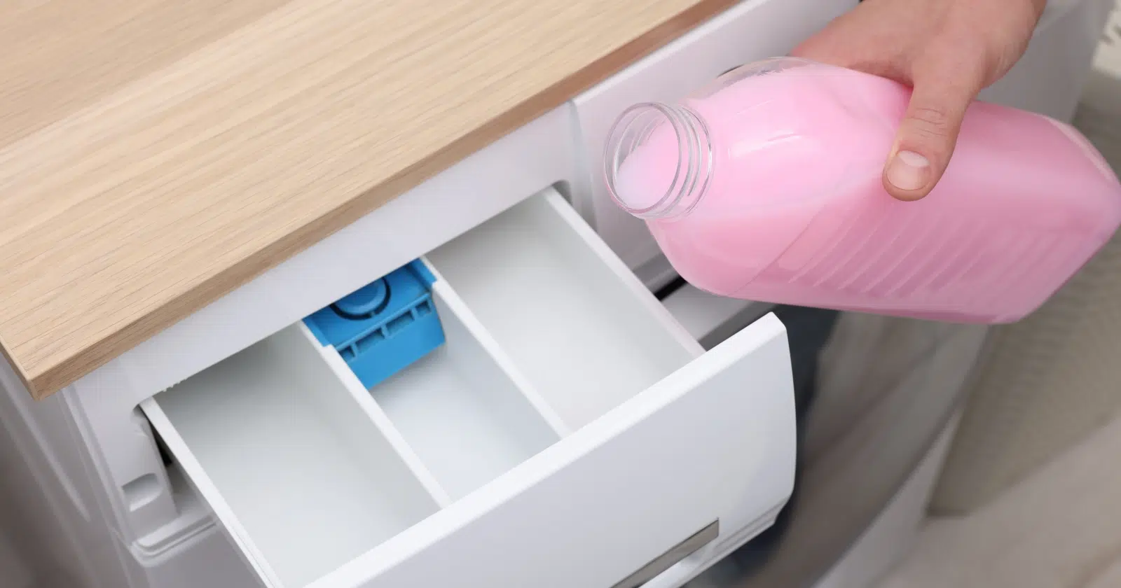 dłoń trzyma detergent i pokazuje, gdzie wlać płyn do prania, a gdzie do płukania w szufladzie pralki